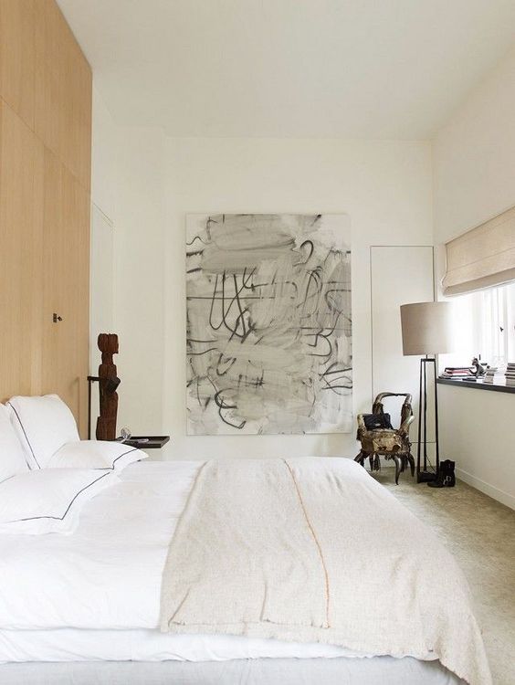 a neutral bedroom with light-colored furniture and lamps, with a wooden accent wall and some bold and dramatic art