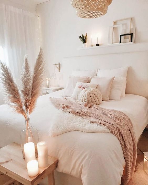 a neutral boho bedroom with white furniture, a woven lamp, pampas grass and candles