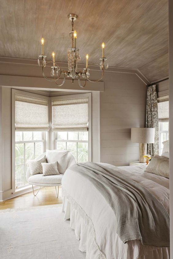 a neutral chalet bedroom with a vintage crystal chandelier, neutral furniture and bedding and pretty lamps