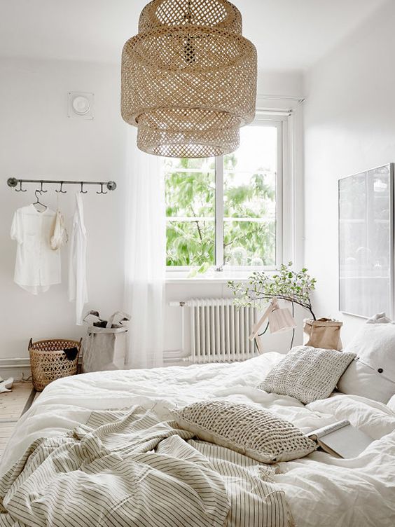 a neutral Scandinavian bedroom with white furniture, a pendant woven lamp, neutral bedding and some greenery