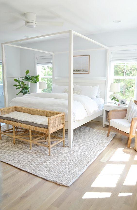 a stylish modern neutral bedroom with a white canopy bed, a woven bench, chairs and neutral textiles