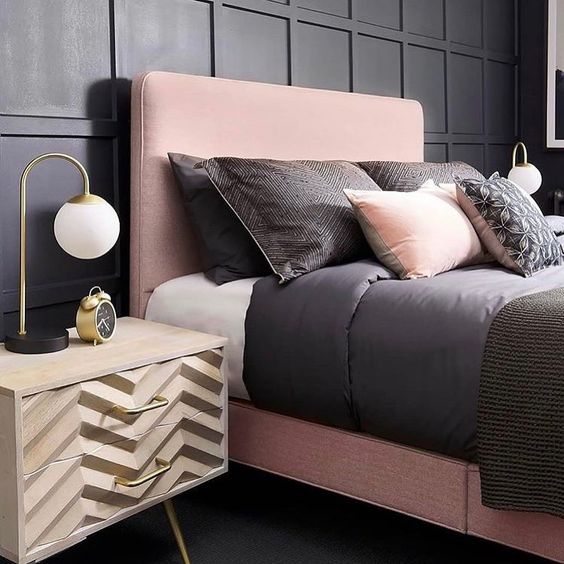 a chic bedroom with black paneling, a pink bed, black and pink bedding and chevron nightstands plus touches of gold