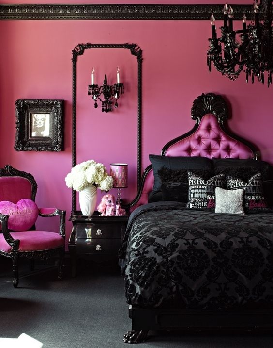 a dramatic black and pink bedroom with bright pink walls, a chair, a pink bed, a black chandelier, bedding and frames