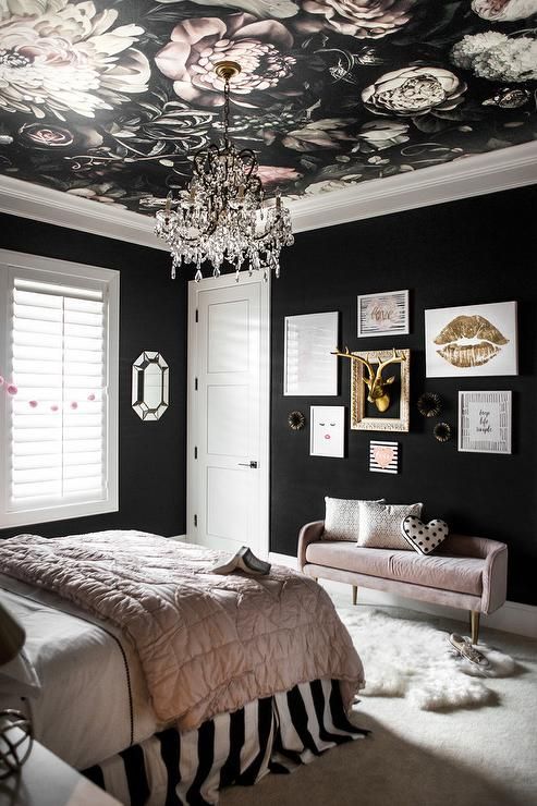 a modern glam bedroom with black walls, a floral ceiling, blush and black bedding and a chic gallery wall