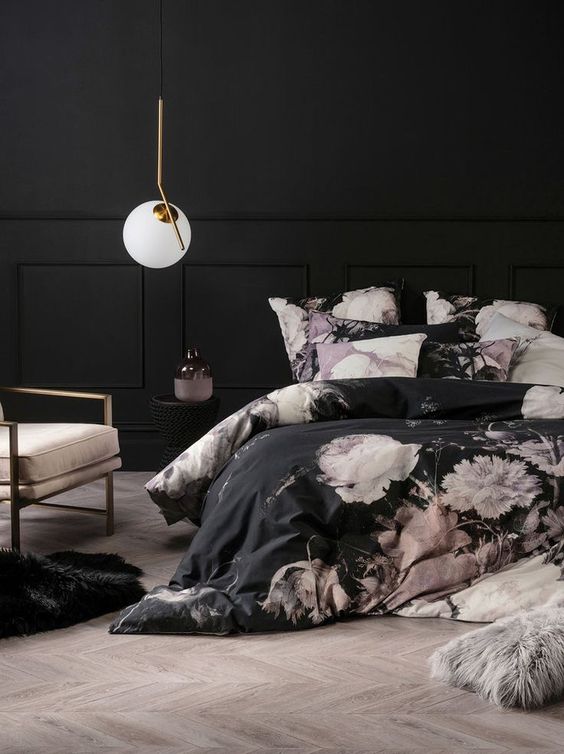 a very refined bedroom with black walls, paneling, black and pink floral bedding, a blush chair and a pendant lamp