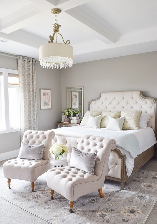 a beautiful and sophisticated greige bedroom with creamy upholstered furniture, neutral pillows, pritned curtains and a rug, a pendant lamp with crystals and mirrors