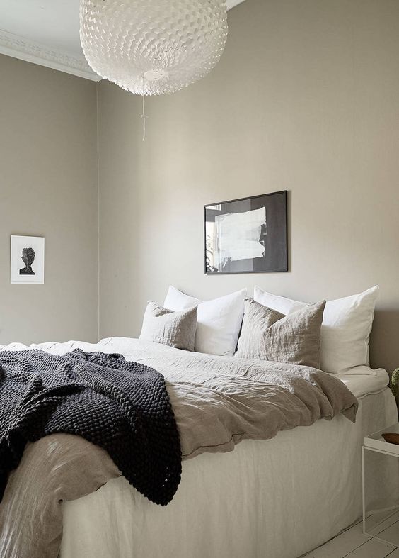 a greige bedroom with a large bed, lightweight nightstands, a beautiful pendant lamp and some lovely black and white artworks