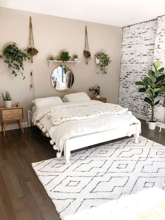 a lovely bedroom with a greige accent wall and a whitewashed brick one, a white bed with creamy bedding, stained nightstands and potted greenery