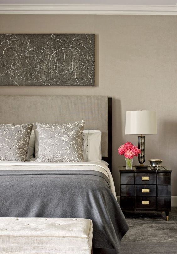 a refined greige bedroom with a greige bed, black elegant nightstands, an upholstered bench and an abstract artwork over the bed