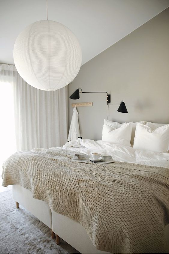 an ethereal greige bedroom with a creamy bed, a black sconce, a pendant lamp and neutral textiles is welcoming