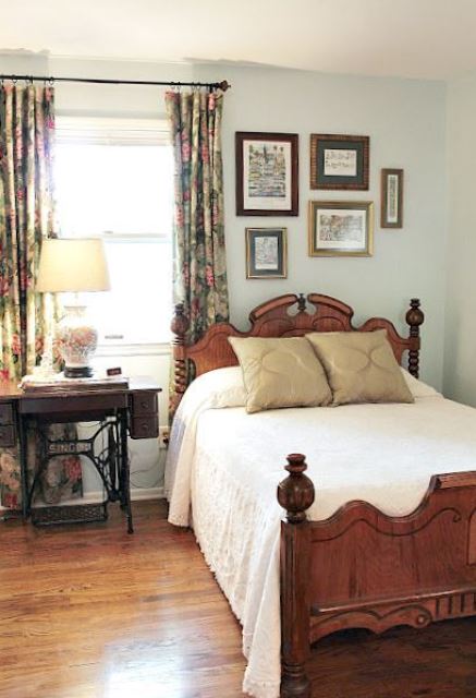 a cozy vintage bedroom with light blue walls, heavy furniture, a chic gallery wall and a floral lamp