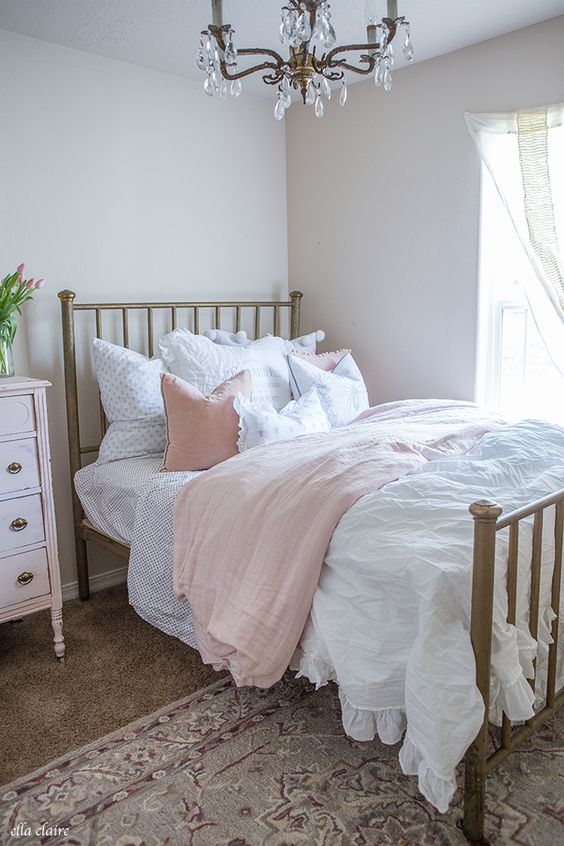 a neutral bedroom with a metal bed, a crystal chandelier, a blush sideboard and blush and white bedding