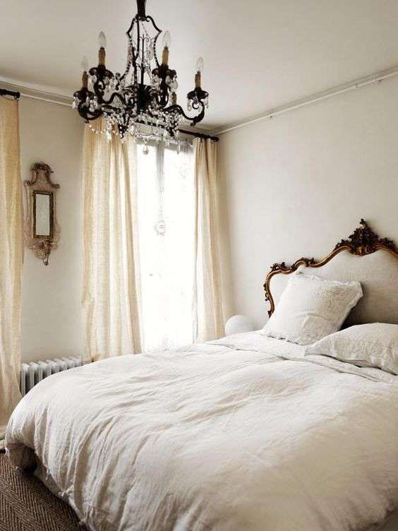 a neutral bedroom with printed textiles, a crystal chandelier, vintage furniture and beautiful framing