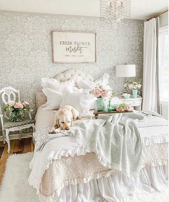 a pastel vintage bedroom with a printed wallpaper wall, a refined bed and nightstands, printed bedding and a crystal chandelier