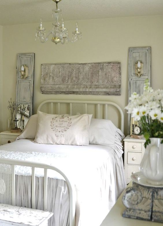 a pastel vintage bedroom with light green walls, a metal bed, neutral furniture, whitewashed decor and a fringe piece plus a crystal chandelier