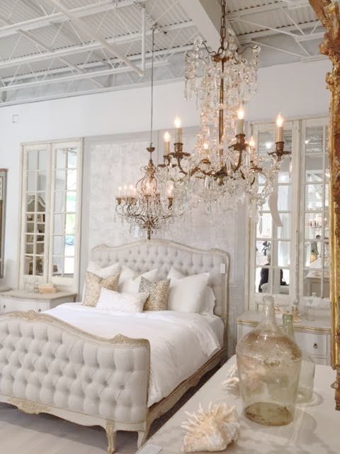 a refined neutral bedroom with a chic bed, crystal chandeliers, mirrors and printed pillows