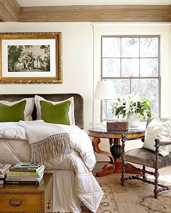 a refined vintage bedroom with a grey bed, heavy furniture, neutral bedding, green pillows, a vintage chest and blooms