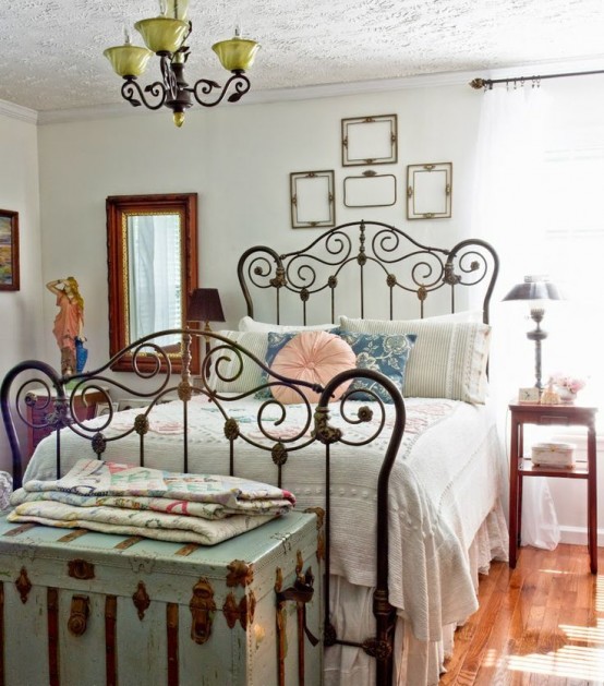 a vintage bedroom with white walls, vintage furniture and a forged bed, a mint chest at the foot and a gallery wall