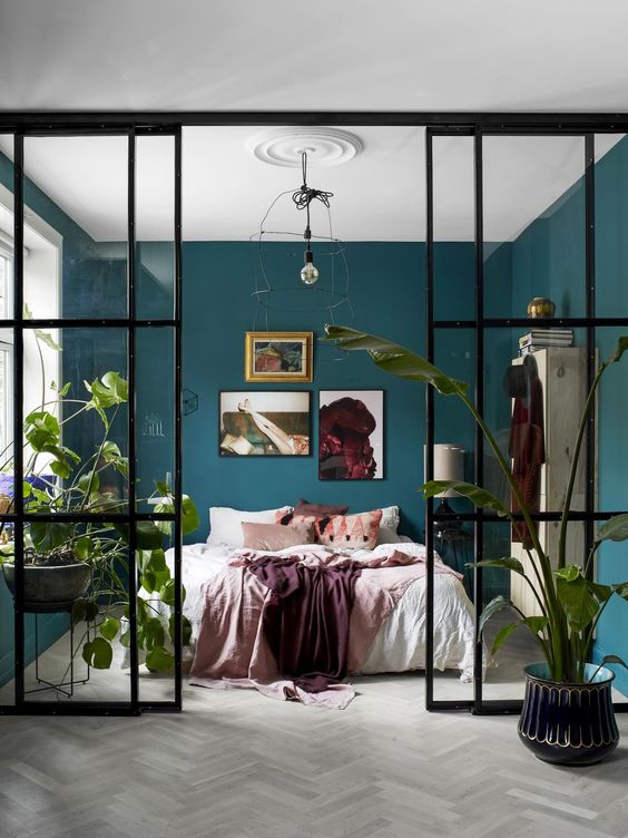 a cozy bedroom with a bed, a vintage storage unit and some bold art, with hunter green walls and a glass wall with doors