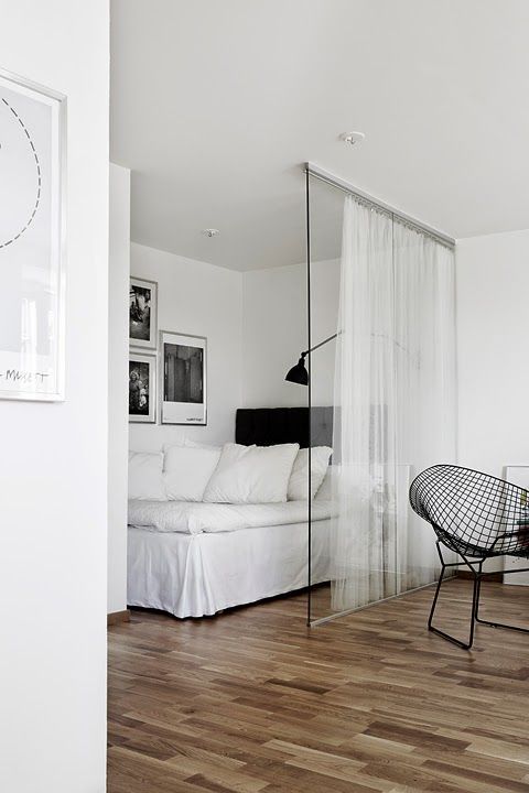 a Nordic bedroom with a bed and some black and white artworks separated from the rest of the apartment with a glass sliding door