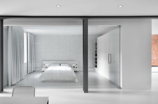 a super clean and minimalist bedroom in white, with an exposed brick wall, storage units and curtains is very airy and a glass wall connects it to the rest of the house