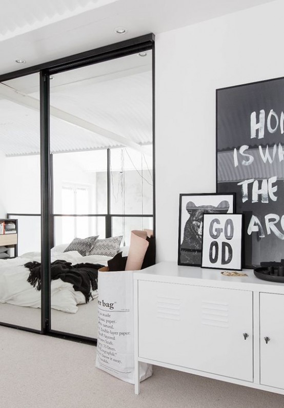 a monochromatic Scandinavian bedroom with a bed right on the wall, storage units and some sheer glass walls to bring some light inside