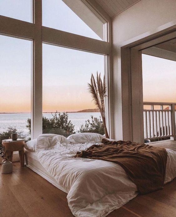 a relaxed neutral bedroom with a framed glazed wall, stylish furniture, pampas grass and a wooden nightstand is very cool