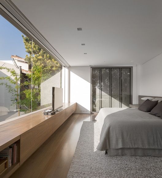 a minimalist bedroom with storage hidden in the wall, a bed, a sleek storage unit and a glass wall with a view of a private courtyard