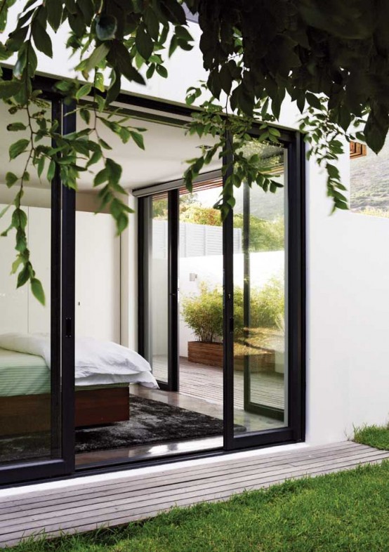 a simple and modern bedroom with a rug and abed and glass walls everywhere gets much daylight and cool views at the same time