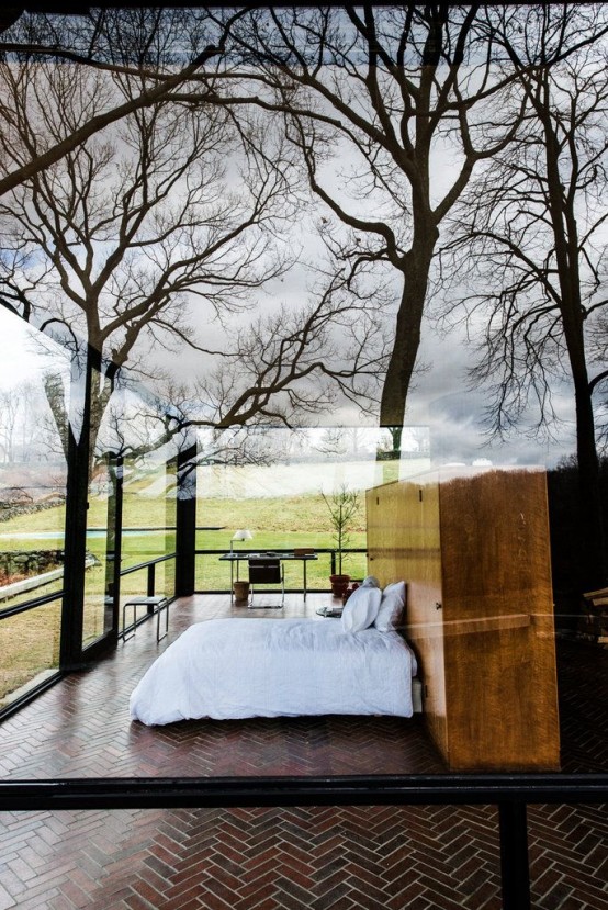 a mid-century modern bedroom with tiles on the floor, a wooden storage unit, a home office nook and all glass walls around to enjoy the moors