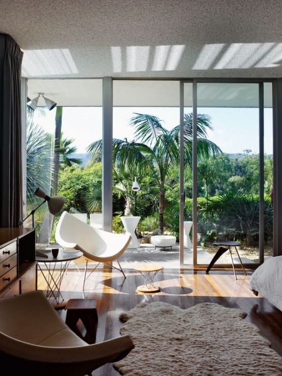 a tropical mid-century modern bedroom with stylish furniture and a glass wall that separates the room the garden and provides cool views