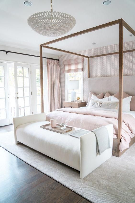 a beautiful feminine bedroom with a wallpaper accent wall, a canopy bed, blush bedding and curtains and a chic chandelier