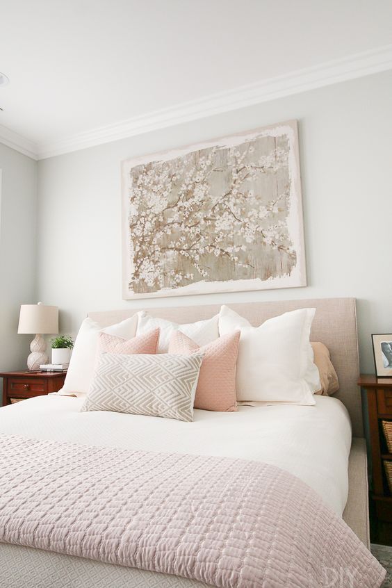 a chic feminine bedroom with grey walls, an upholstered bed, neutral and pastel bedding, wooden nightstands and a floral artwork