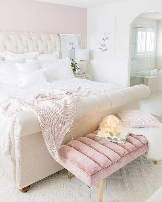 a pretty girlish bedroom done in white and light pink, with an upholstered bed and a pink bench, white bedding and lights