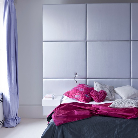 a minimalist bedroom with white walls, a lavender upholstered headboard, lavender curtains, fuchsia pillows and a blanket is very chic