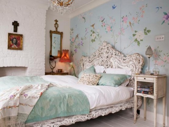 an eclectic feminine bedroom with a blue floral painted wall, a white carved bed and nightstands, a faux fireplace and artworks is very catchy