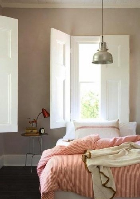 a mid-century modern neutral bedroom with a cool nightstand, a red lamp, a bed with pink striped bedding and cozy blankets is very chic