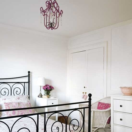 a beautiful feminine bedroom with a black metal bed, a purple crystal chandelier, touches of pink and lilac and some printed bedding