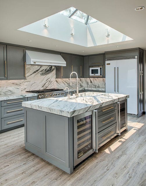 Luxury kitchen design in a classic style with a skylight over the island, gray kitchen fronts, marble worktop and splash protection wall, modern built-in refrigerator in white