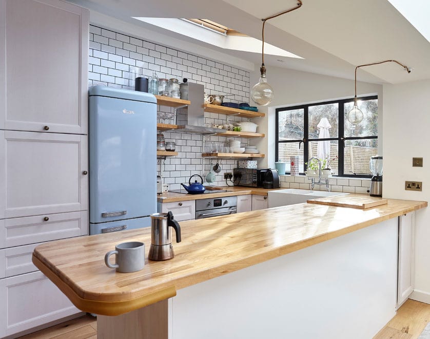 attractive furnishing idea for small kitchens in vintage style with retro fridge in light blue, metro wall tiles white, wooden wall shelves and breakfast bar