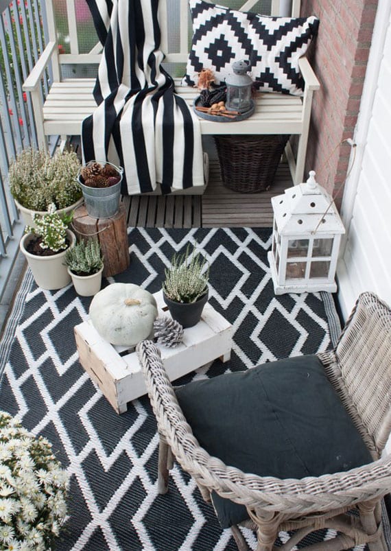 balcony in autumn chic design with carpet and blanket in black and white, white autumn flowers and natural decoration with cones, pumpkin and wood