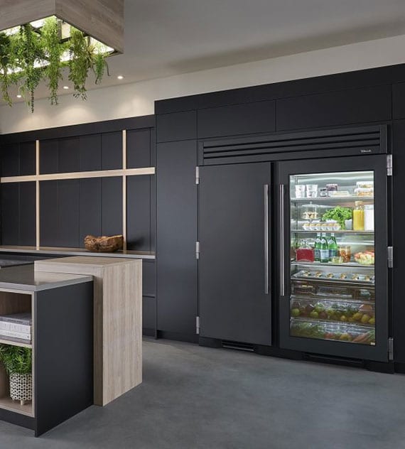 modern black built-in kitchen with side-by-side refrigerator as built-in device with glass door and attractive ceiling lamp with greenery over the kitchen island