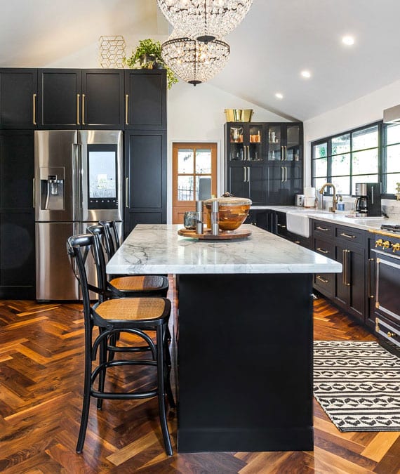 attractive kitchen design in black and brass combination with parquet floor in herringbone pattern, crystal chandeliers above the dining counter made of marble and smart sidy by side refrigerator samsumg