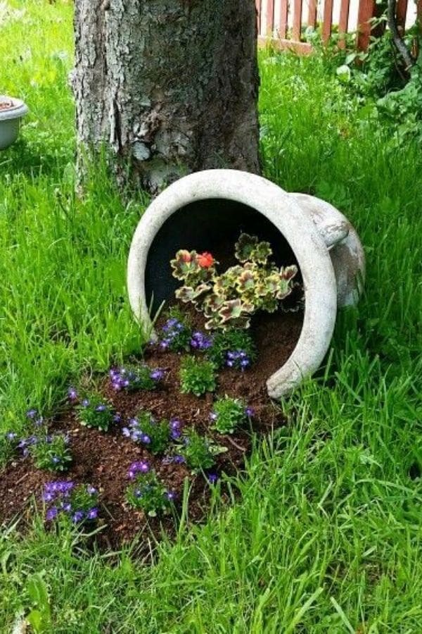 White urn with purple flowers by tree